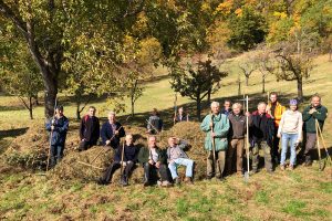 ca. 15 Menschen mit Rechen vor einem großen Haufen Gras an einer herbstlichen Wiese